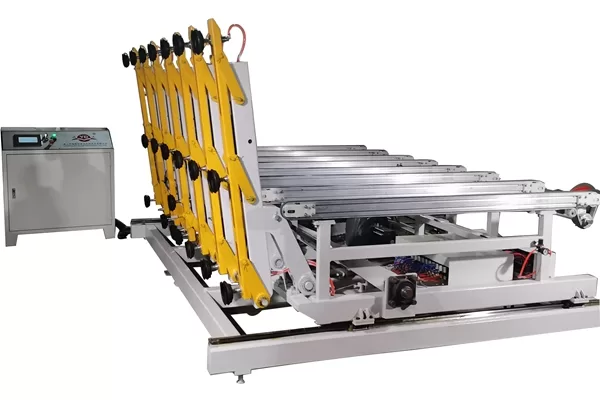 A studio shot showing the loading machine in a partially raised position, emphasizing the yellow mechanical arm linkages and the integration with the conveyor table.